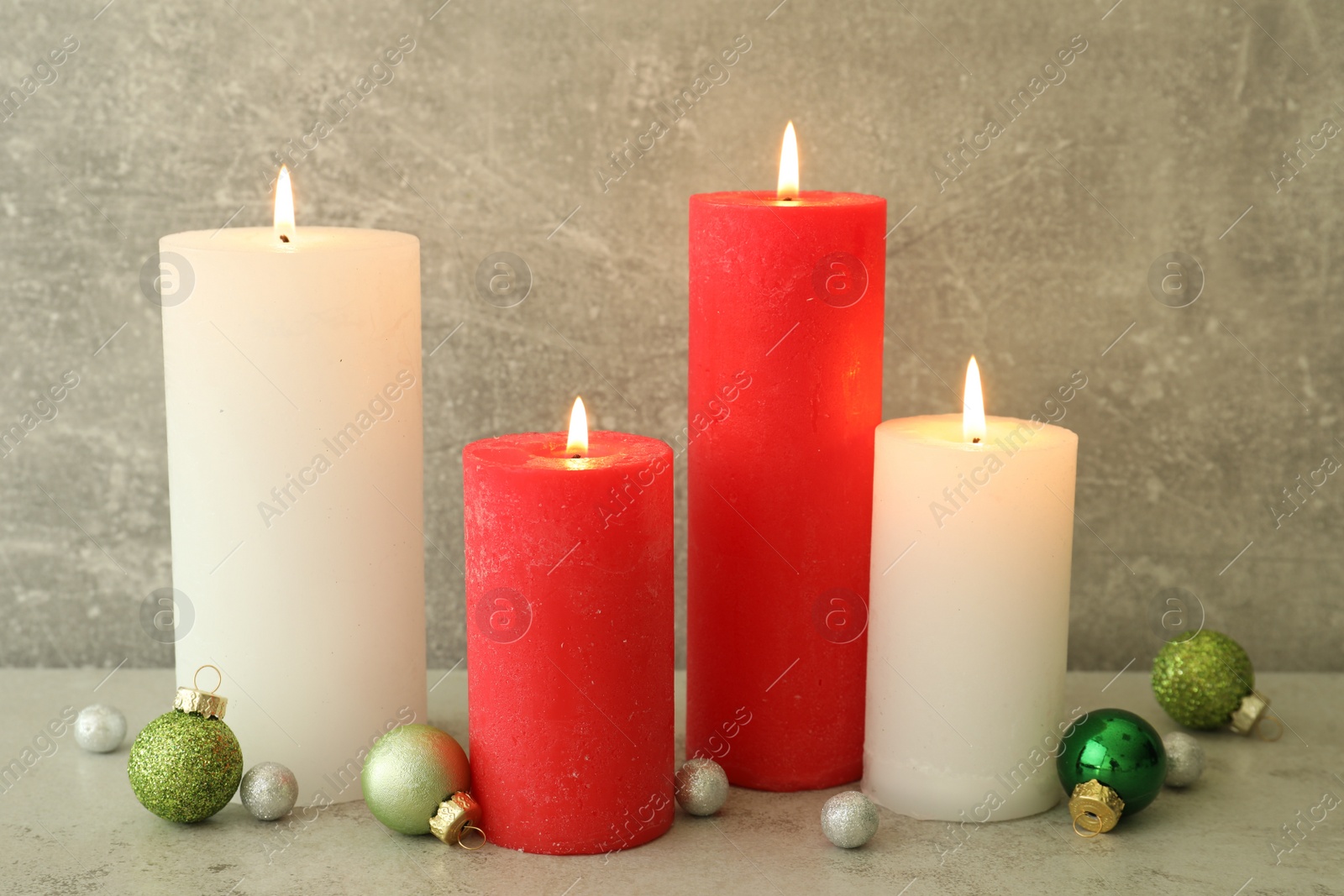 Photo of Burning candles with Christmas baubles on light grey table