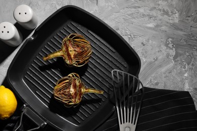 Pan with tasty grilled artichokes on grey textured table, flat lay