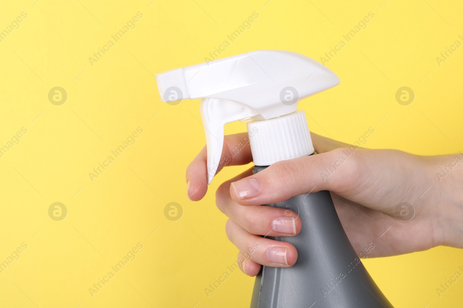 Photo of Woman holding plastic spray bottle on yellow background, closeup. Space for text