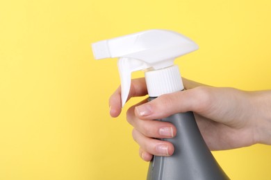 Photo of Woman holding plastic spray bottle on yellow background, closeup. Space for text