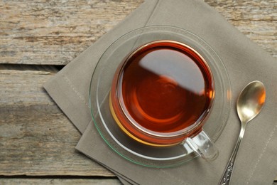 Aromatic tea in glass cup, spoon and napkin on wooden table, top view