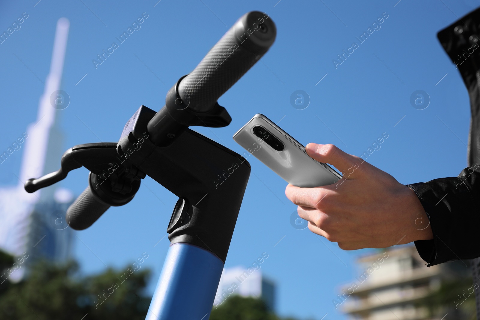 Photo of Man using smartphone to pay and unblock rental electric scooter outdoors, closeup