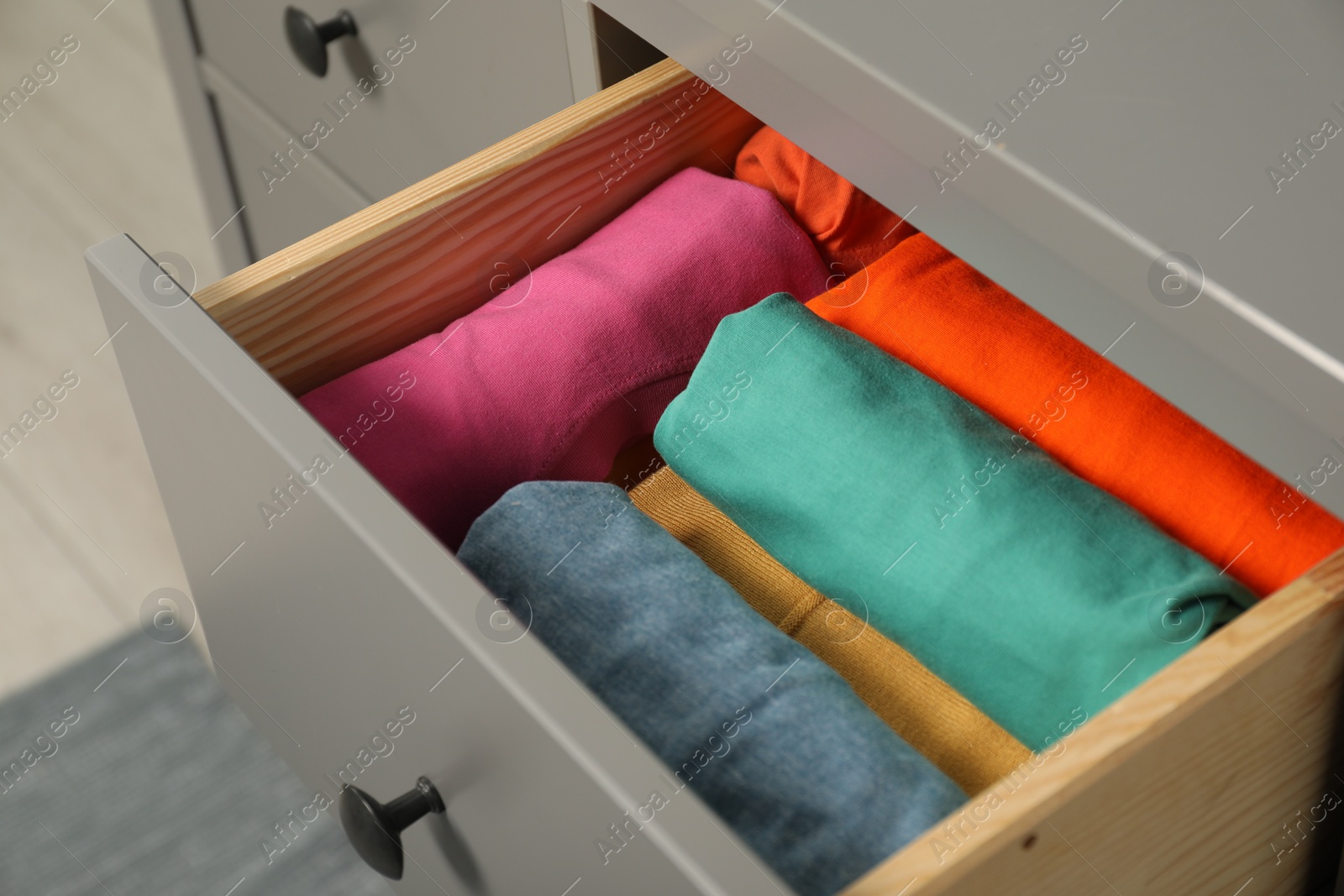 Photo of Different rolled shirts in drawer indoors. Organizing clothes