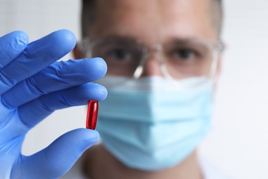 Photo of Doctor holding pill on light background, selective focus. Space for text