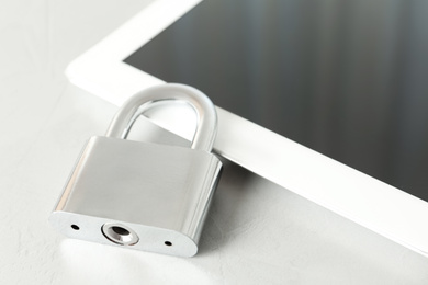 Metal lock and tablet on light grey table, closeup. Protection from cyber attack