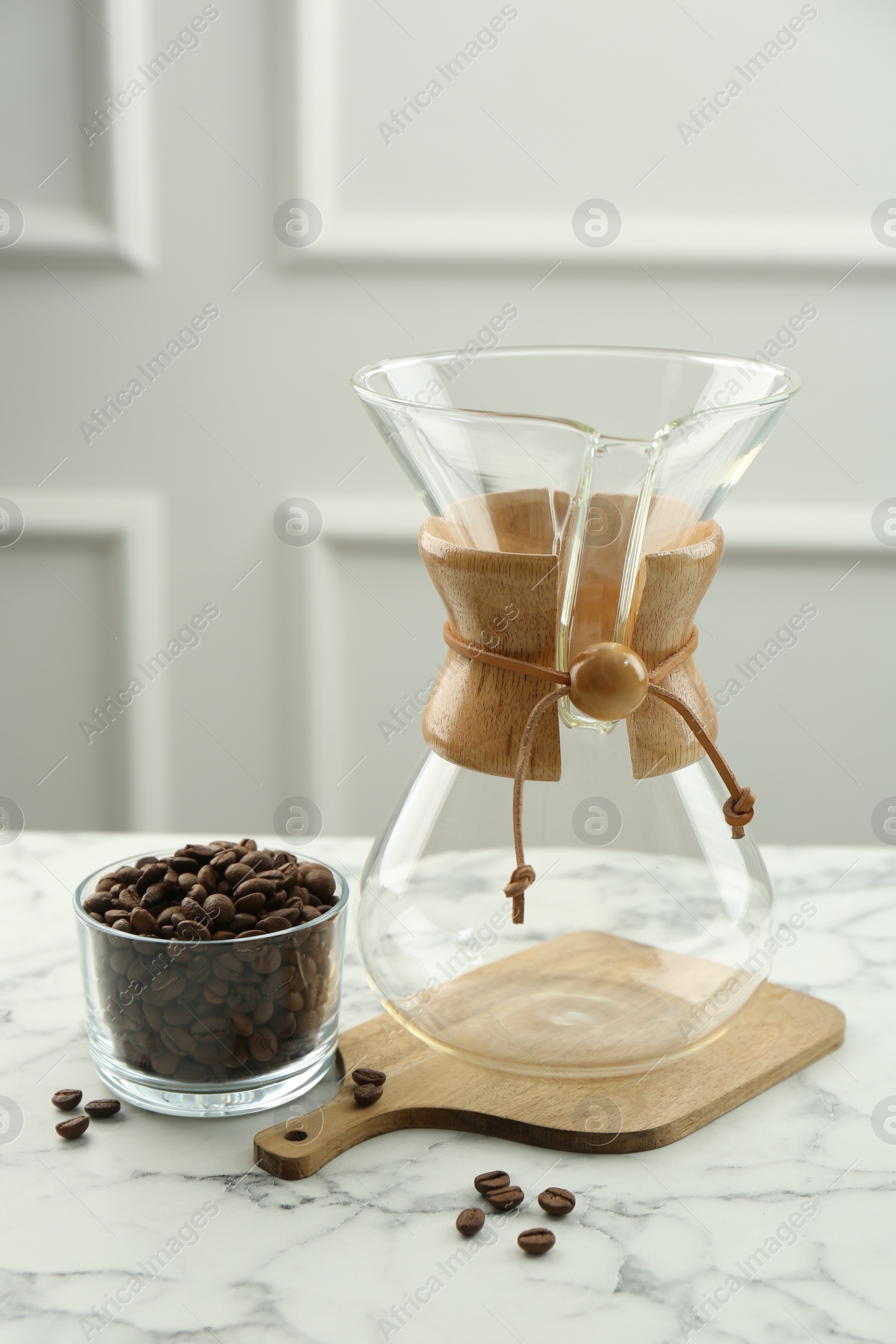 Photo of Empty glass chemex coffeemaker and beans in bowl on white marble table