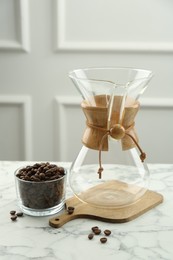 Empty glass chemex coffeemaker and beans in bowl on white marble table