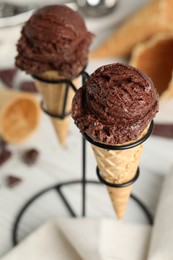 Photo of Chocolate ice cream scoops in wafer cones on stand, closeup