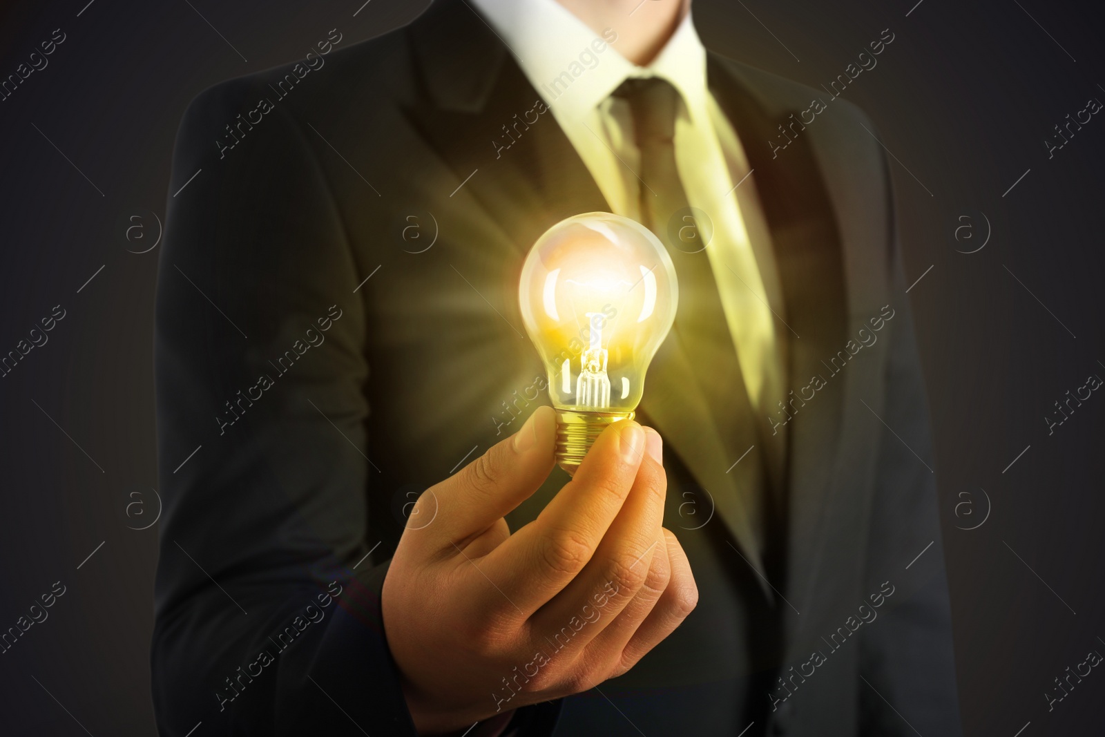 Image of Glow up your ideas. Businessman holding light bulb on dark background, closeup