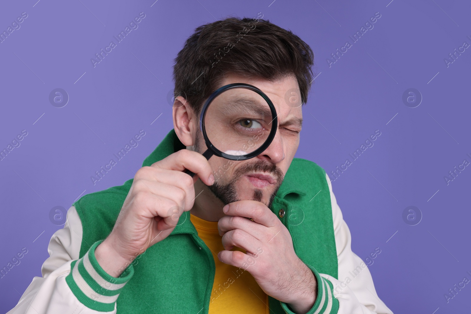 Photo of Confused man looking through magnifier glass on purple background