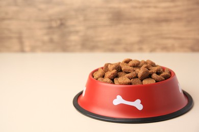 Photo of Dry dog food in feeding bowl on beige table. Space for text