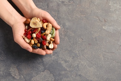 Woman holding handful of different dried fruits and nuts on color background, top view. Space for text