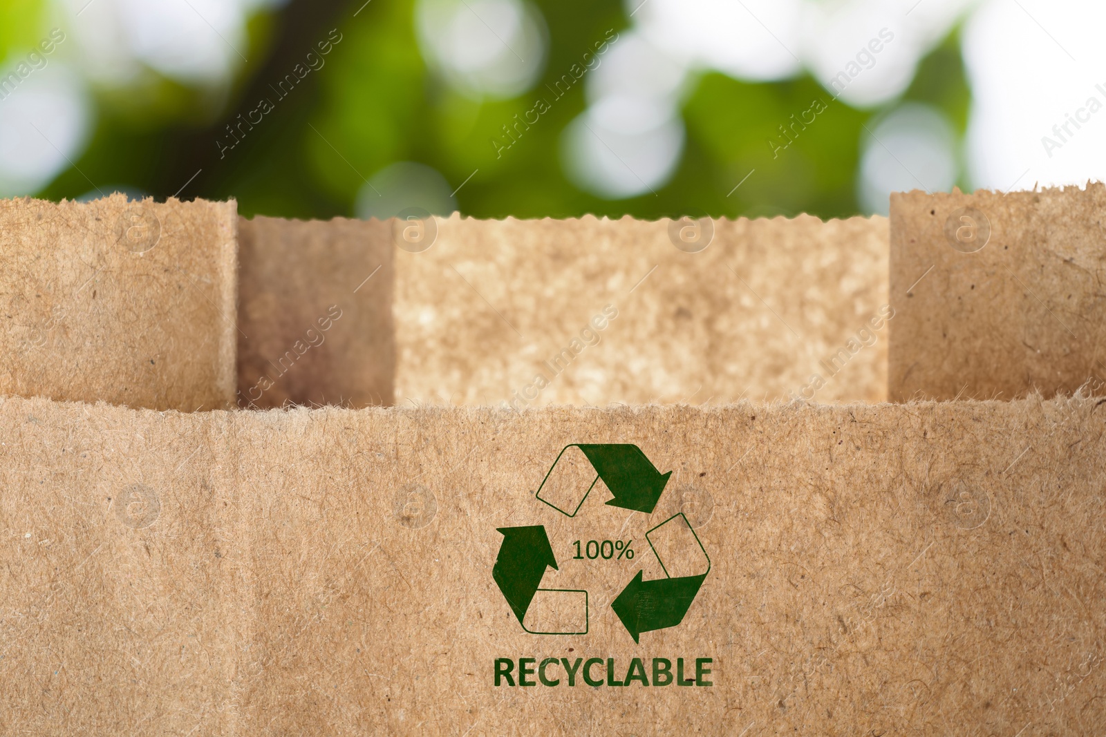 Image of Paper bag with recycling symbol on blurred green background. Eco friendly package