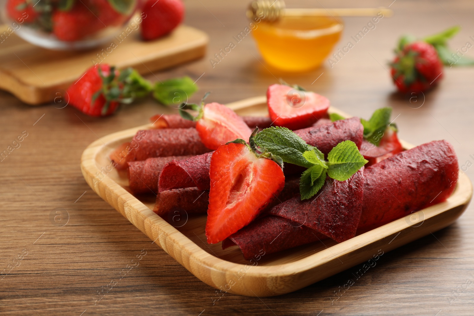 Photo of Delicious fruit leather rolls and strawberries on wooden table, closeup