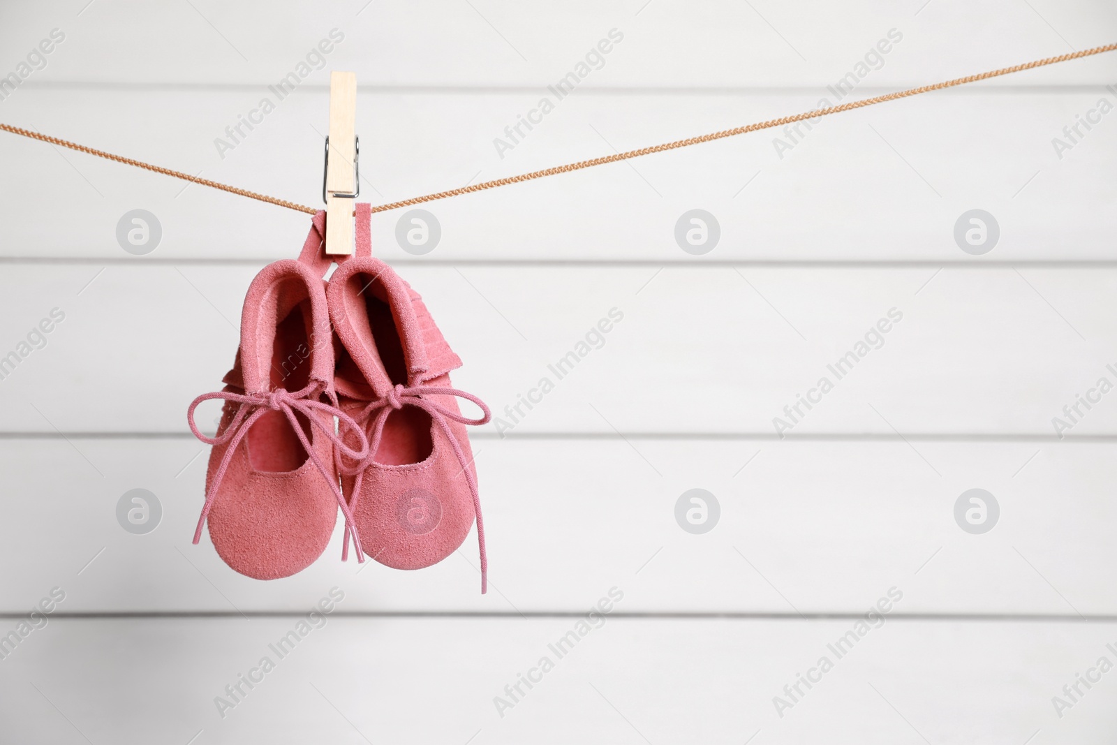 Photo of Pink baby shoes drying on washing line against white wall. Space for text