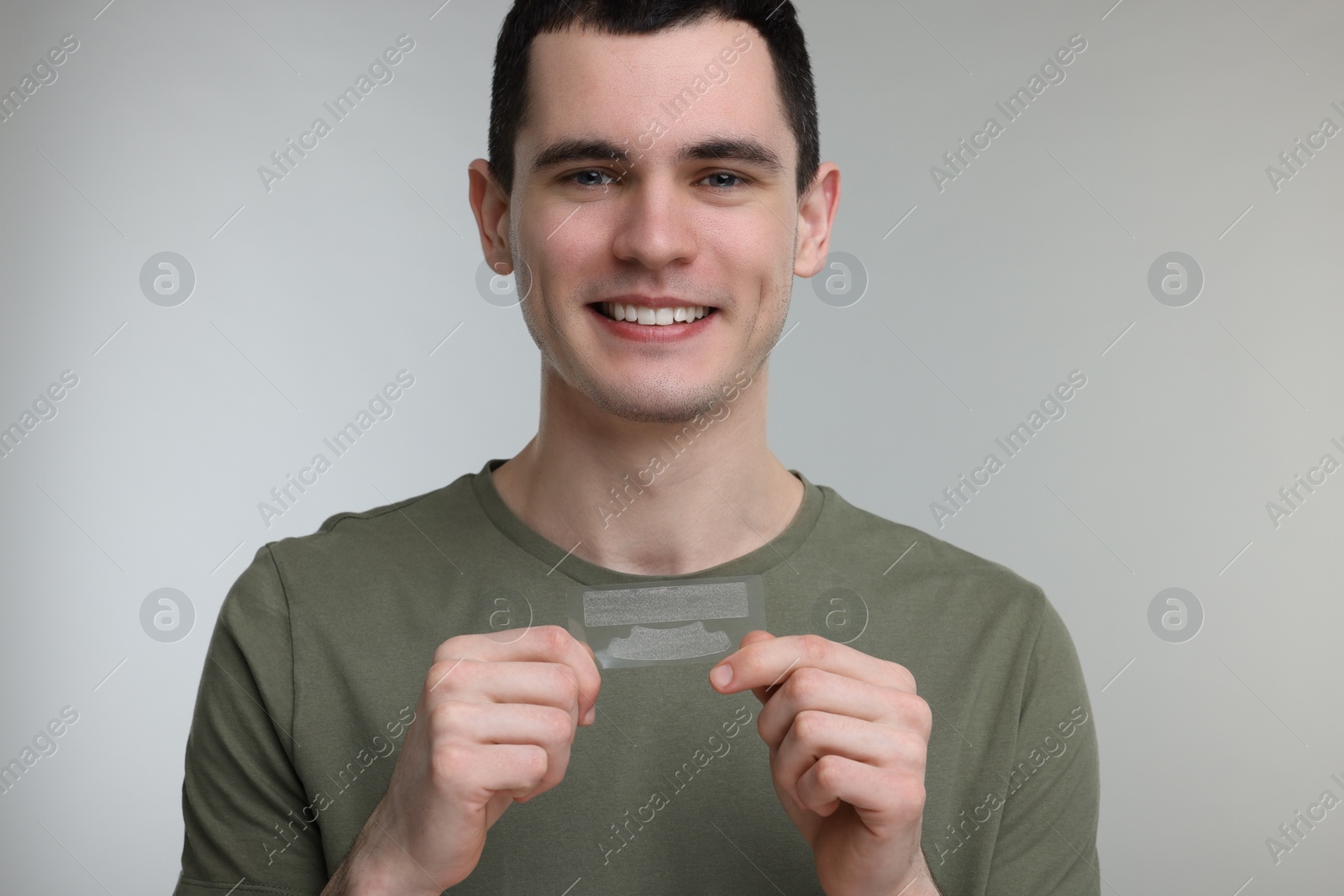 Photo of Young man with whitening strips on light grey background