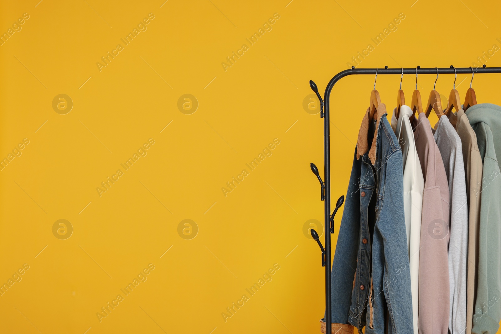 Photo of Rack with stylish clothes on wooden hangers against orange background, space for text