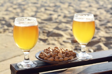 Photo of Glasses of cold beer and pistachios on wooden table outdoors