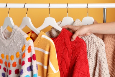 Woman choosing sweater on rack against color background, closeup