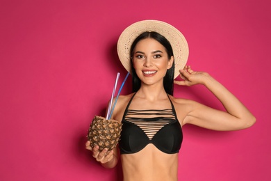 Beautiful young woman in black bikini with cocktail on pink background