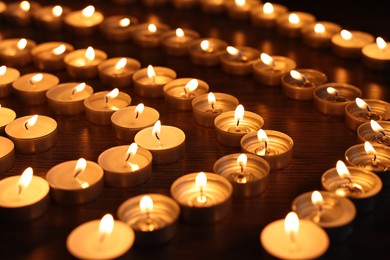 Photo of Burning candles on wooden table in darkness