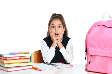 Photo of Emotional little girl in uniform with school stationery at desk against white background