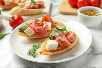 Photo of Plate of tasty bruschettas with prosciutto on table