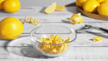Photo of Bowl with peel pieces, fresh lemons and zester on white wooden table