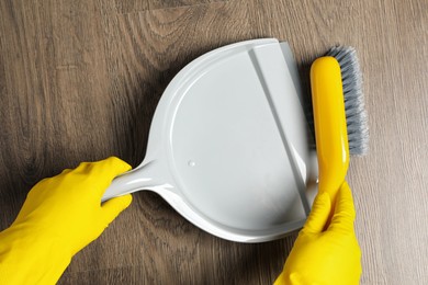 Woman in gloves sweeping wooden floor with plastic whisk broom and dustpan, top view