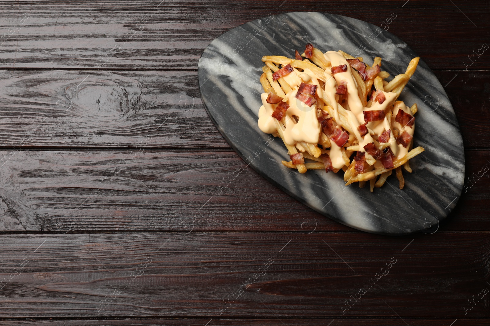 Photo of Delicious French fries with bacon and cheese sauce on wooden table, top view. Space for text