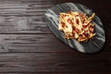 Delicious French fries with bacon and cheese sauce on wooden table, top view. Space for text