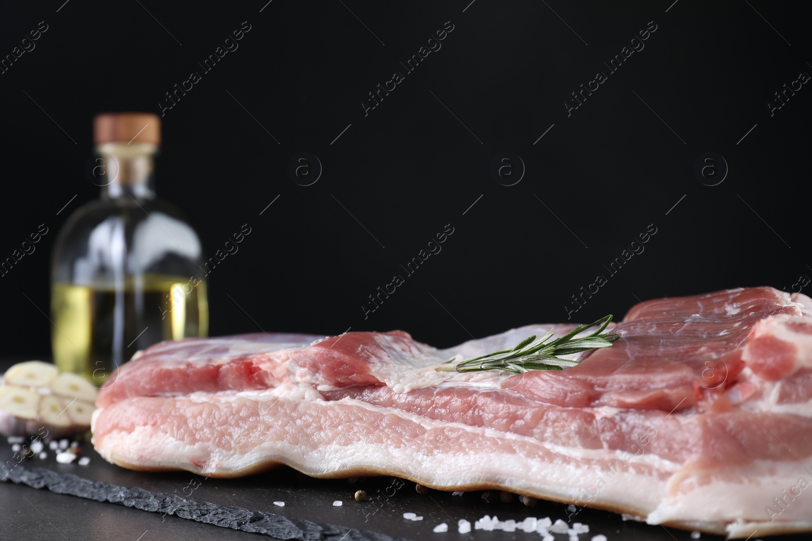 Photo of Piece of raw pork belly, rosemary and salt on grey table, closeup