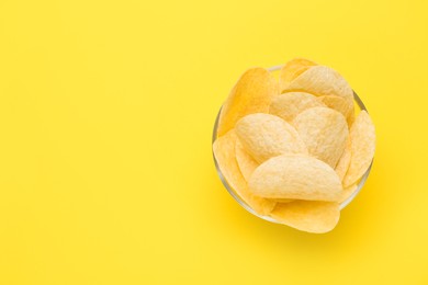 Photo of Bowl of tasty potato chips on yellow background, top view. Space for text