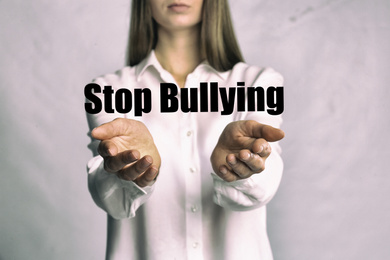 Image of Young woman showing sign STOP BULLYING on light background, closeup