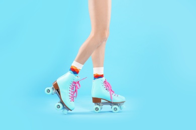 Young woman with retro roller skates on color background, closeup