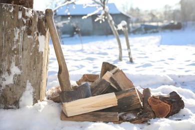 Metal axe and pile of wooden logs outdoors on sunny winter day