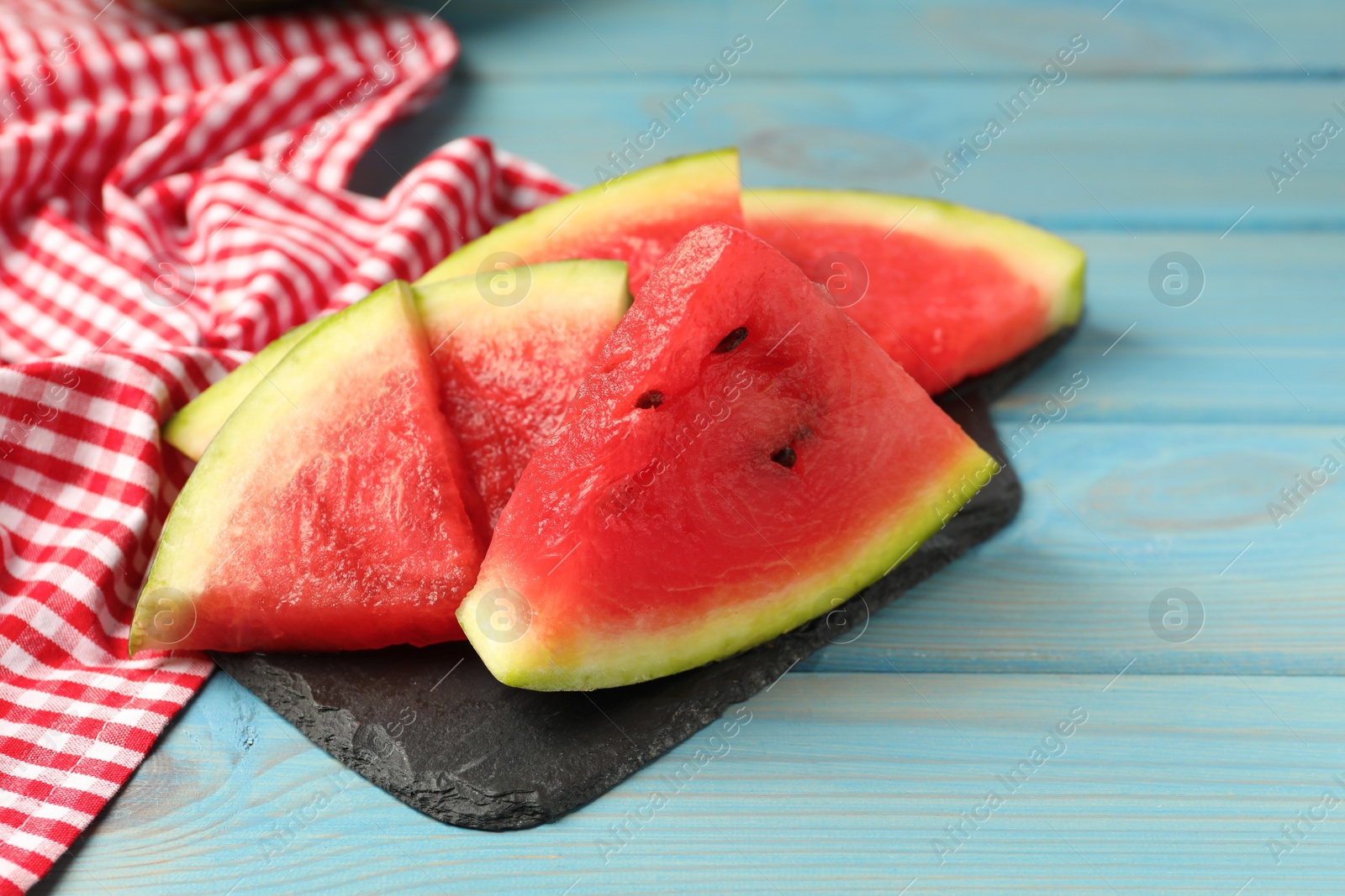 Photo of Slate board with slices of juicy watermelon on light blue wooden table