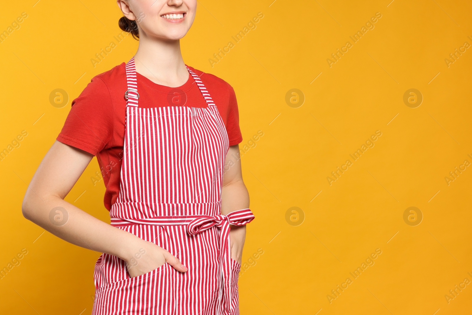 Photo of Woman in clean striped apron on orange background, closeup. Space for text