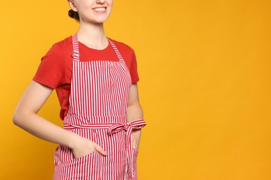 Photo of Woman in clean striped apron on orange background, closeup. Space for text