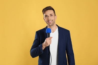 Photo of Young male journalist with microphone on yellow background