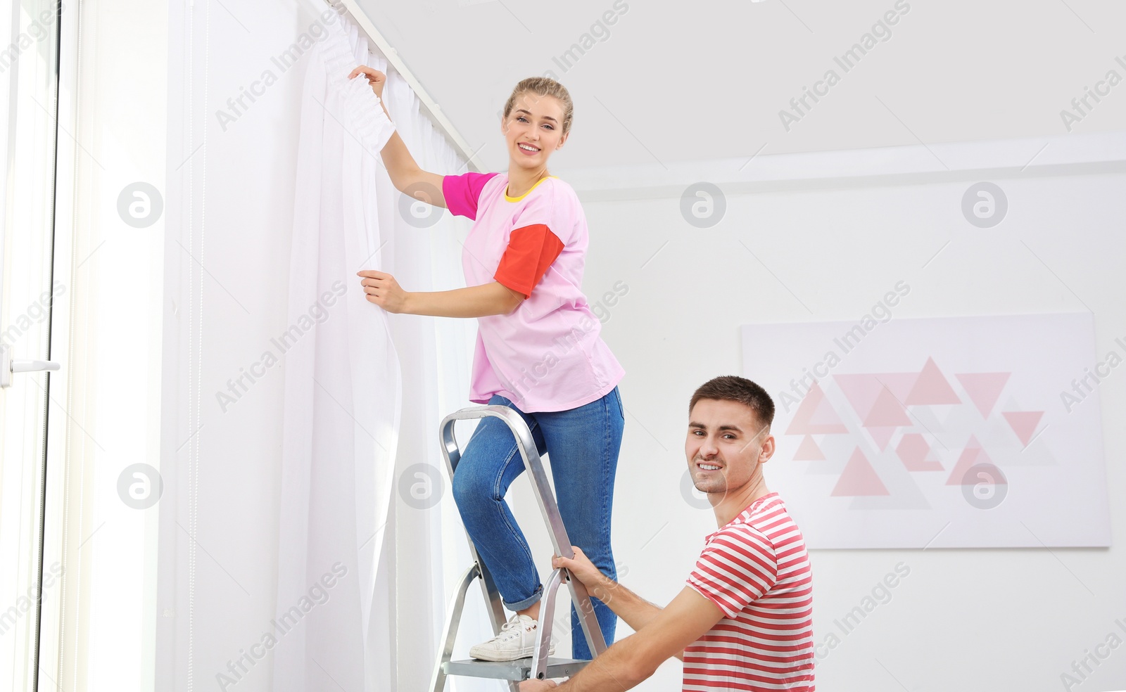 Photo of Young couple hanging window curtain indoors. Interior decor element