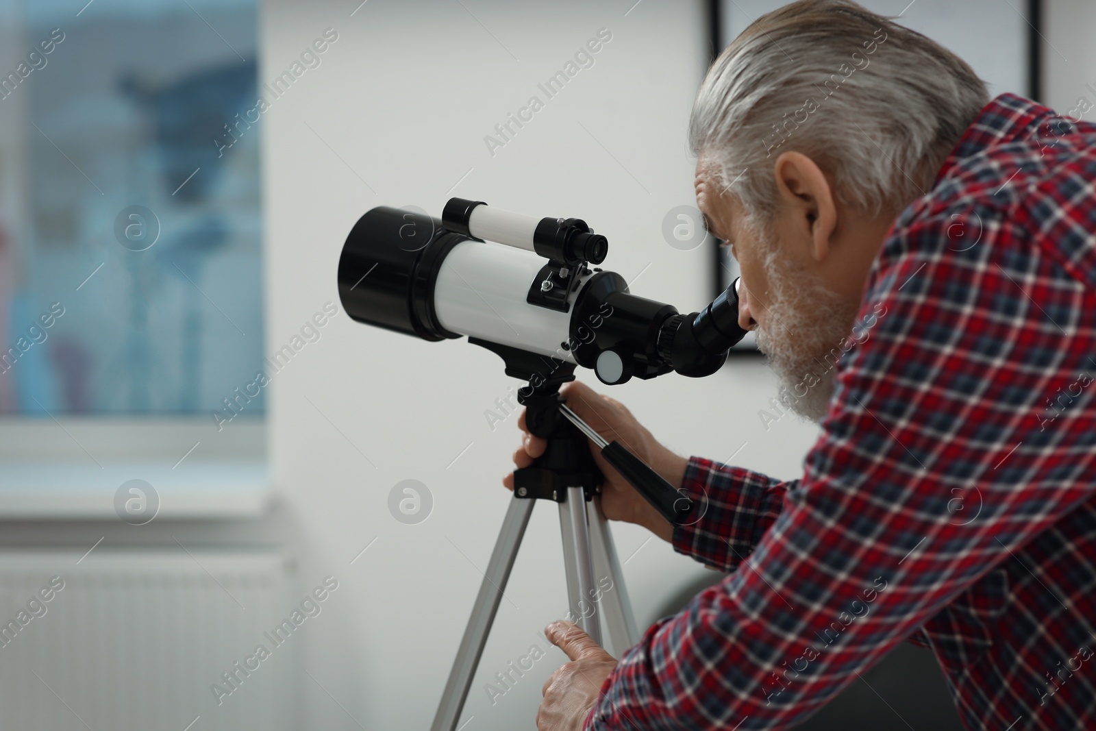 Photo of Senior man looking at stars through telescope in room