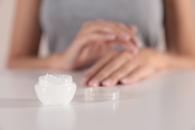 Photo of Young woman at table, focus on jar with cream