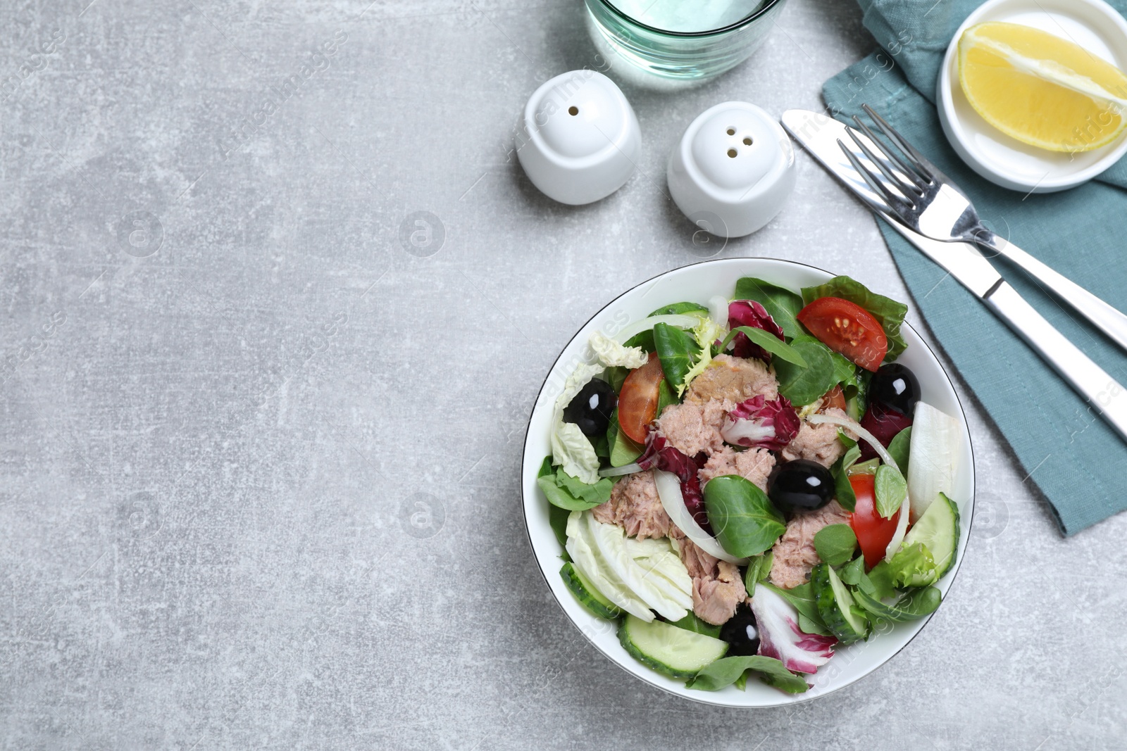 Photo of Bowl of delicious salad with canned tuna and vegetables served on light grey table, flat lay. Space for text