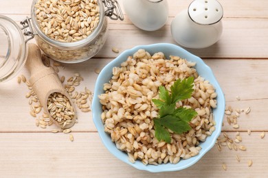 Delicious pearl barley with parsley served on wooden table, flat lay