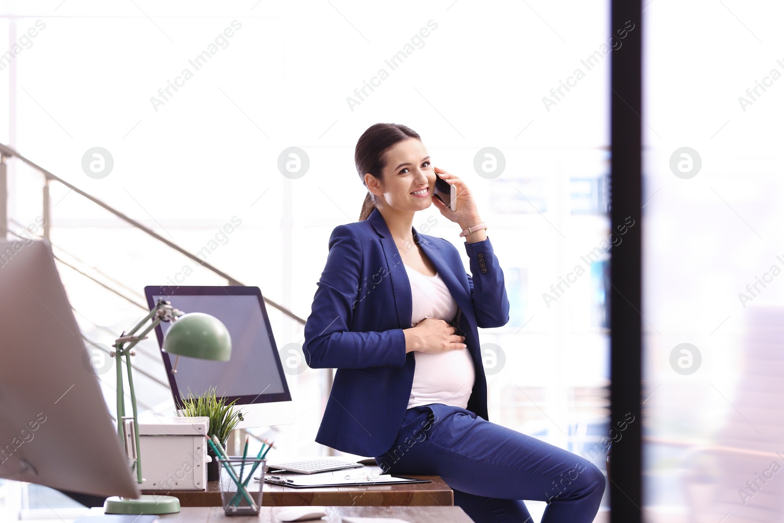 Photo of Young pregnant woman talking on phone while working in office