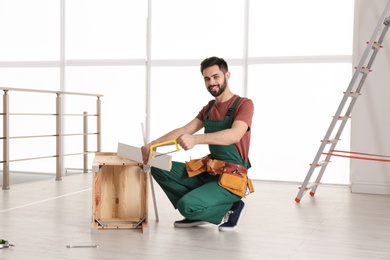 Carpenter in uniform making furniture indoors. Professional construction tools