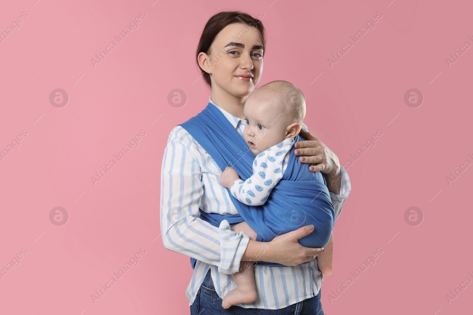 Photo of Mother holding her child in sling (baby carrier) on pink background