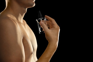 Photo of Young man using perfume on black background, closeup. Space for text