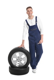 Male mechanic with car tires on white background